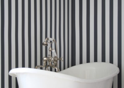Vintage Revival of soaking tub with dramatic black and white pin stripe wallpaper